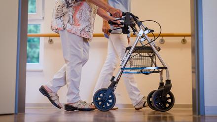 Eine Pflegekraft geht in einem Pflegeheim mit einer älteren Dame über einen Korridor. 