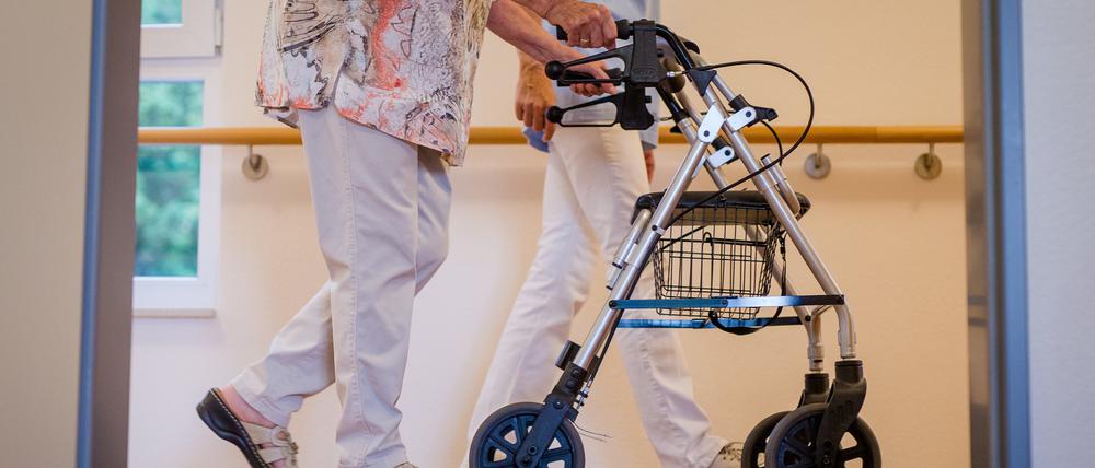 Eine Pflegekraft geht in einem Pflegeheim mit einer älteren Dame über einen Korridor. 