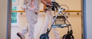 Eine Pflegekraft geht in einem Pflegeheim mit einer älteren Dame über einen Korridor. 