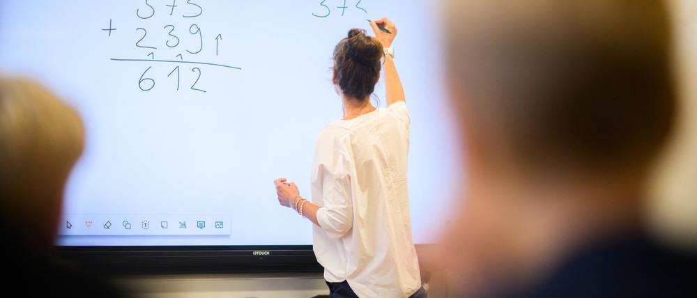 ARCHIV - 17.08.2023, Niedersachsen, Hannover: Eine Lehrerin schreibt eine Mathematikaufgabe auf eine digitale Schultafel im Klassenraum einer 4. Klasse einer Grundschule in der Region Hannover. (zu dpa: «Gericht bestätigt Vorgriffsstunde für Lehrer in Sachsen-Anhalt») Foto: Julian Stratenschulte/dpa +++ dpa-Bildfunk +++