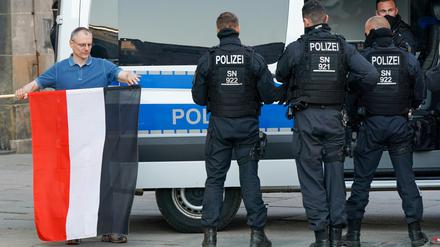 Sachsen, Chemnitz: Ein Mann rollt die Fahne des des Deutschen Reichs neben Polizisten nach der Personalienfeststellung ein.