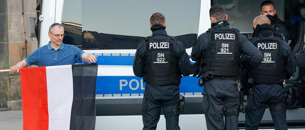 Sachsen, Chemnitz: Ein Mann rollt die Fahne des des Deutschen Reichs neben Polizisten nach der Personalienfeststellung ein.
