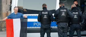 Sachsen, Chemnitz: Ein Mann rollt die Fahne des des Deutschen Reichs neben Polizisten nach der Personalienfeststellung ein.