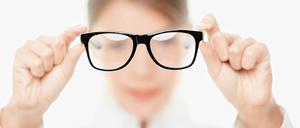 Eine Frau hält eine Brille mit beiden Händen vor ihr Gesicht.