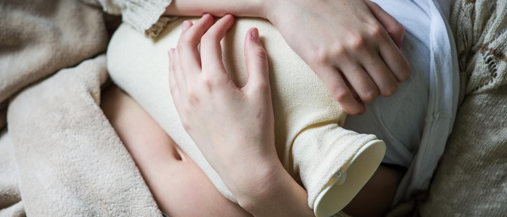 Eine Frau drückt gegen Schmerzen eine Wärmflasche auf ihren Körper.