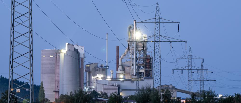 Strommasten stehen im Morgenlicht vor einem Zementwerk in Baden-Württemberg. 