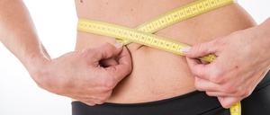 Eine Person legt ein Maßband um ihren flachen Bauch.