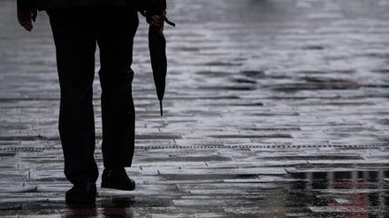 Ein Passant geht mit einem Regenschirm in der Hand durch eine Fußgängerzone.