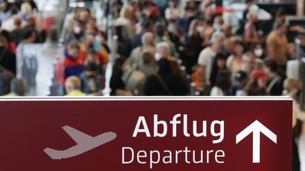 Am Flughafen Berlin Brandenburg BER stehen zahlreiche Reisende in einer Schlange zur Sicherheitskontrolle hinter einem Schild mit der Aufschrift „Abflug“. 