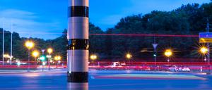 Eine Blitzsäule steht am Kreisverkehr an der Siegessäule, während im Hintergrund vorbeifahrende Fahrzeuge Lichtspuren hinterlassen. (Symbolbild)