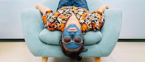 Eine Frau mit Sonnenbrille und Gesichtsmaske fläzt auf einem Sessel.