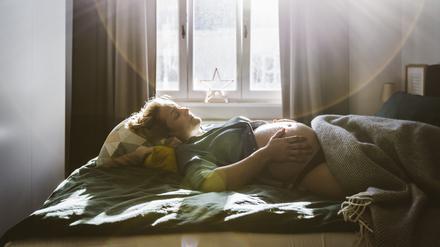 Eine schwangere Frau liegt im Bett und hält ihren nackten Bauch (Symbolbild).