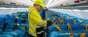 Vor dem letzten Postflug befestigt ein Mitarbeiter der Wisag auf dem BER in einem Airbus A320-214 mit Stoffmanschetten abgedeckte Plastikboxen voller Briefe und anderer Post auf den Passagiersitzen. 