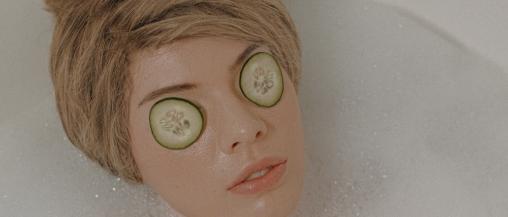 Eine Puppe liegt in einer Badewanne und hat Gurken auf den Augen.