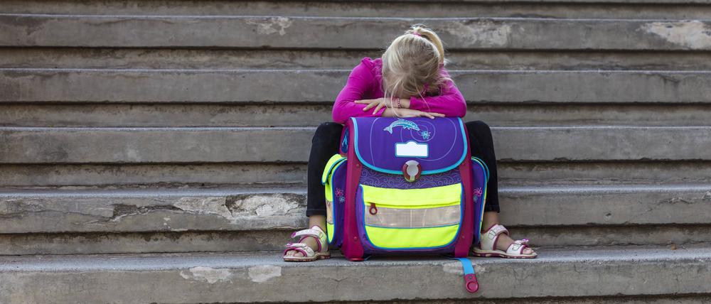 Ein Mädchen sitzt mit Schultasche auf einer Treppe.