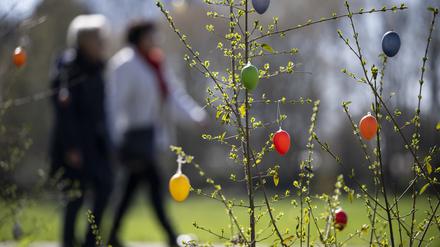 Zwei Menschen laufen an aufgehängten Ostereiern vorbei im Britzer Garten. (Symbolbild)