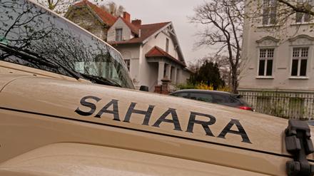 Ein sandfarbener Jeep mit der Aufschrift „Sahara“ steht bei dunstigem Licht in einer Straße in Berlin.