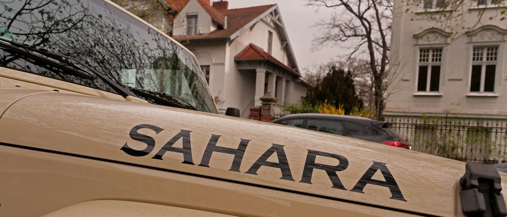 Ein sandfarbener Jeep mit der Aufschrift „Sahara“ steht bei dunstigem Licht in einer Straße in Berlin.