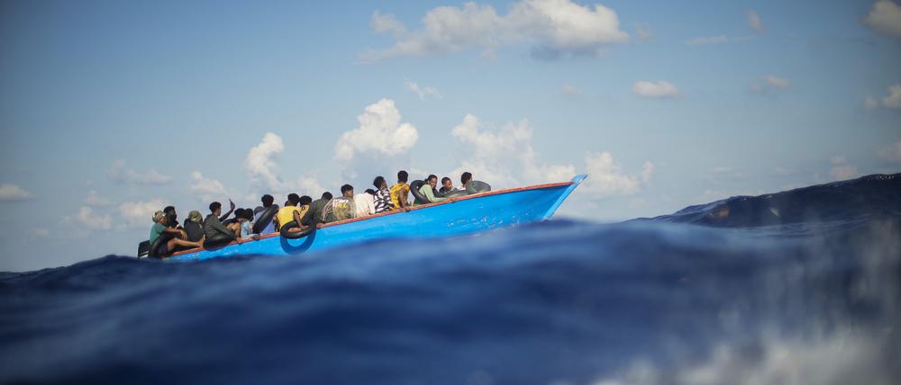 Migranten sitzen in einem Holzboot im Mittelmeer (Symbolbild).