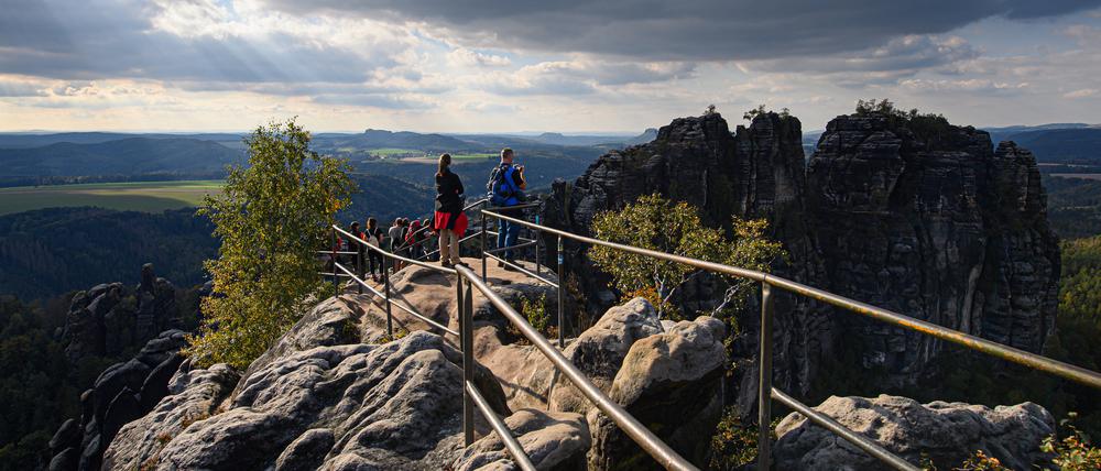 Wanderer blicken von der Schrammsteinaussicht in der Sächsischen Schweiz auf die Felsen der Schrammsteine.
