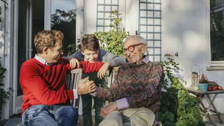 Ein lächelnder Großvater sitzt mit Sohn und Enkelsohn auf der Terrasse. 