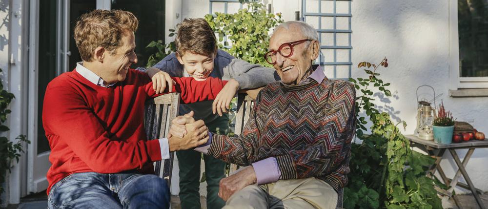 Ein lächelnder Großvater sitzt mit Sohn und Enkelsohn auf der Terrasse.