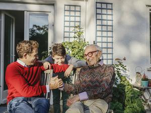 Ein lächelnder Großvater sitzt mit Sohn und Enkelsohn auf der Terrasse. 