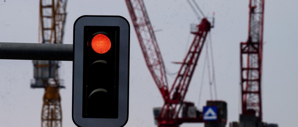 Eine Rot zeigende Ampel vor der Kulisse von Kränen auf einer Baustelle am Alexanderplatz.