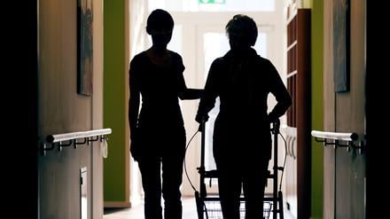  Eine Pflegekraft (l.) begleitet die Bewohnerin eines Altenheims beim Gang über den Flur.
