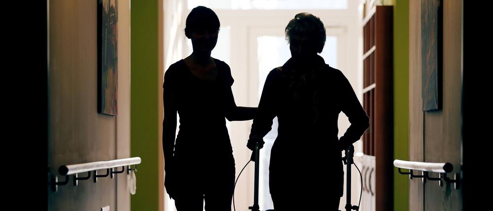  Eine Pflegekraft (l.) begleitet die Bewohnerin eines Altenheims beim Gang über den Flur.