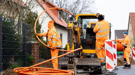 Arbeiter sind mit Bagger und Spaten an einer Straße mit der Erdverlegung von Glasfaserkabeln beschäftigt. +++ dpa-Bildfunk +++
Glasfas