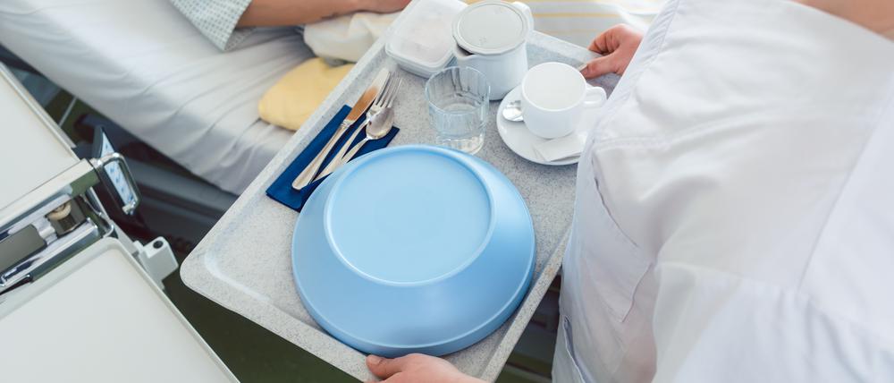 Eine Krankenpflegerin bringt ein Tablett mit Essen ans Bett einer Patientin.