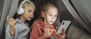 Curious boy with headphones looking at sister using mobile phone in tent at home model released, Symbolfoto property released, NJAF00836