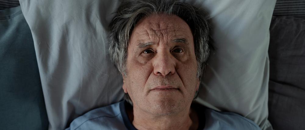 Ein Mann liegt mit offenen Augen im Bett.