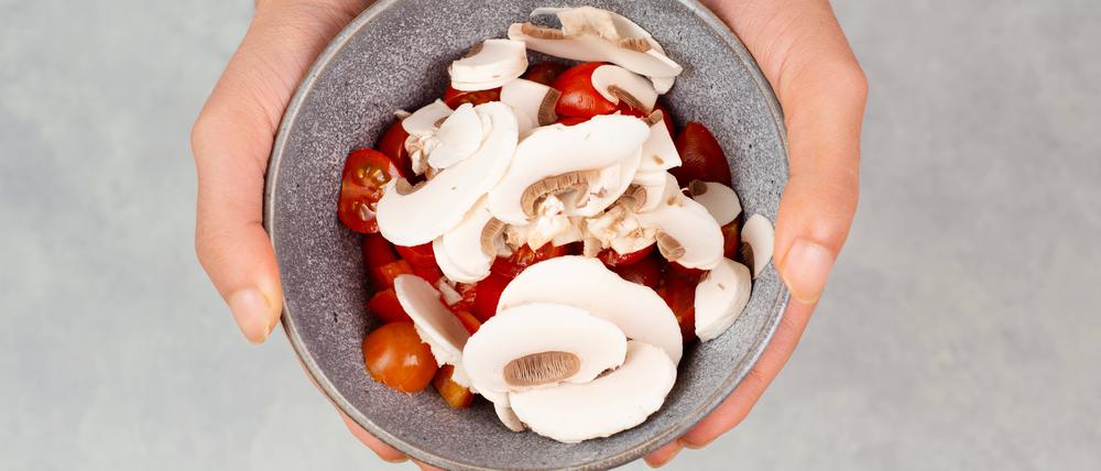 Eine Person hält eine mit Tomaten und Pilzen gefüllte Schüssel in den Händen.