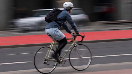 Ein Fahrradfahrer mit Helm fährt über einen Radweg an der Straße