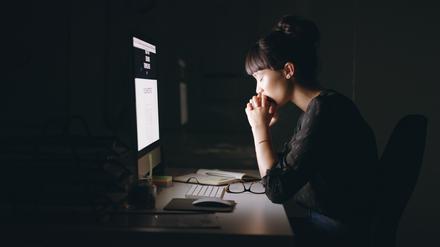 Shot of a young businesswoman sitting with her hands clasped while working on a computer in an office at night