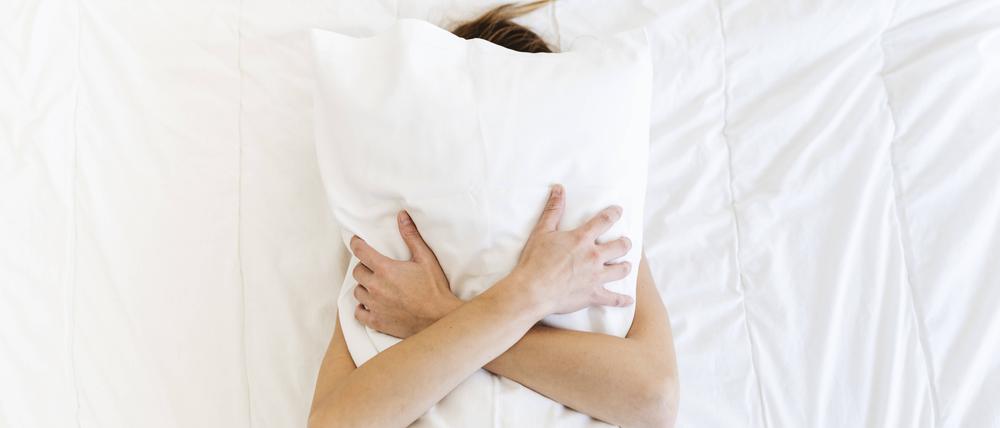 Eine Frau liegt rücklings auf dem Bett und umklammert ihr Kopfkissen.