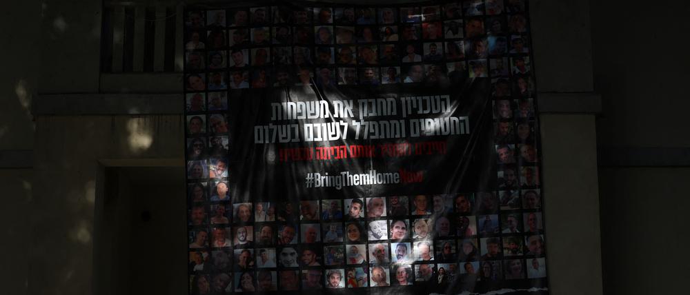 Aus dem Dunkel leuchtet ein großes Plakat mit den Gesichtern der israelischen Geiseln an einer Hauswand in Tel Aviv.