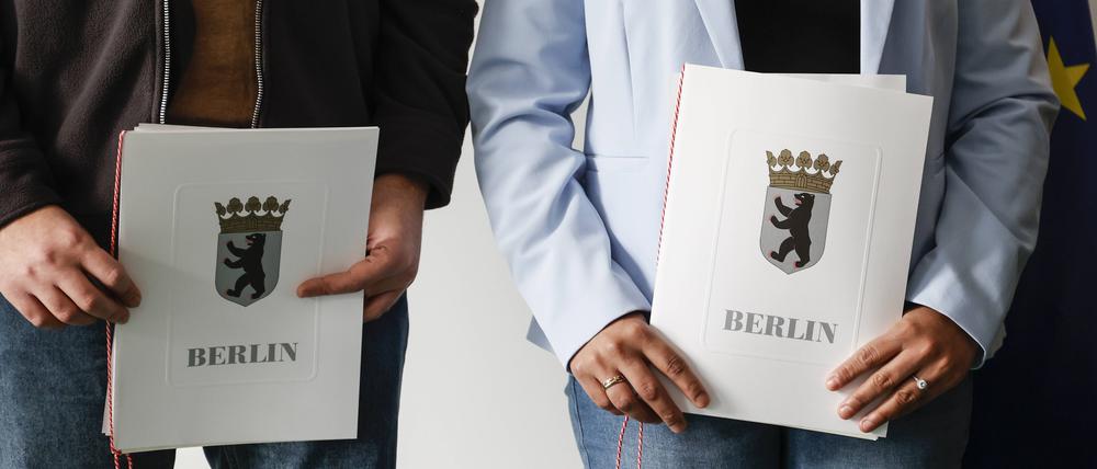 Eingebürgerte zeigen ihre Urkunden nach einer Feier bei der Zentralen Einbürgerungsstelle des Landesamtes für Einwanderung.