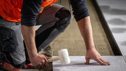 Ein Bauarbeiter verlegt mit einem Gummihammer den Bodenbelag auf einer Baustelle.