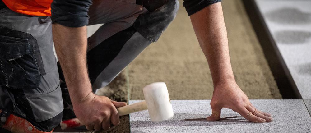 Ein Bauarbeiter verlegt mit einem Gummihammer den Bodenbelag auf einer Baustelle.