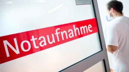Ein Krankenpfleger steht in einem Krankenhaus neben einer Glastür mit der Aufschrift „Notaufnahme“ (Symbolbild).