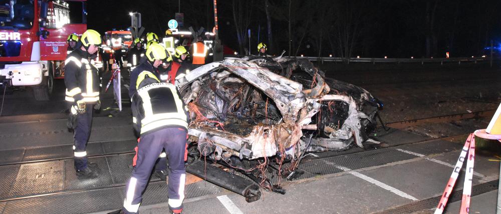 Rettungskräfte stehen am Wrack eines zerstörten Autos nach einem Unfall an einem Bahnübergang. Ein Mensch ist beim Zusammenstoß eines Autos mit einem Zug an einem Bahnübergang in Bestensee (Landkreis Dahme-Spreewald) ums Leben gekommen.