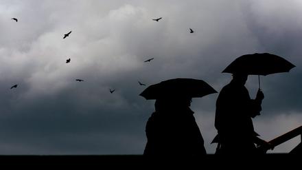Passanten gehen mit Regenschirmen durch eine Stadt.