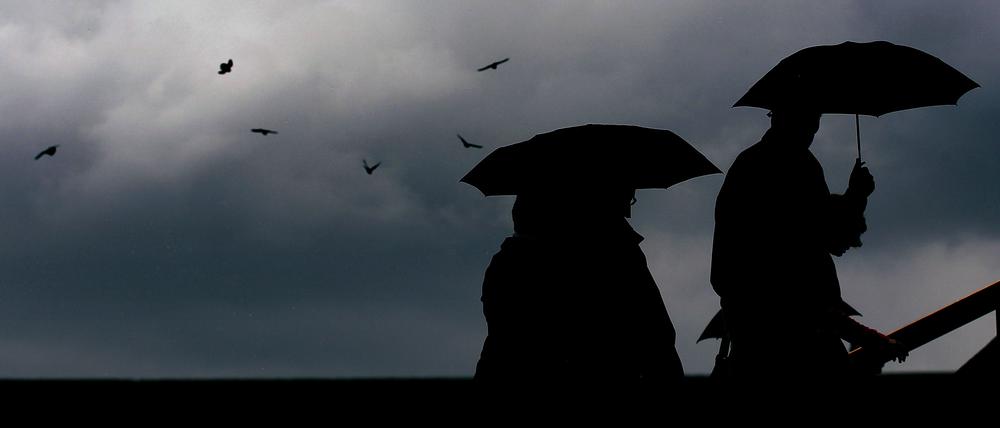 Passanten gehen mit Regenschirmen durch eine Stadt.