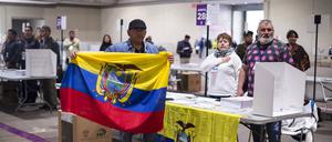 Tischdelegierte mit einer ecuadorianischen Flagge singen die Nationalhymne auf dem IFEMA-Messegelände in Madrid, während des Tages des Referendums in Ecuador.