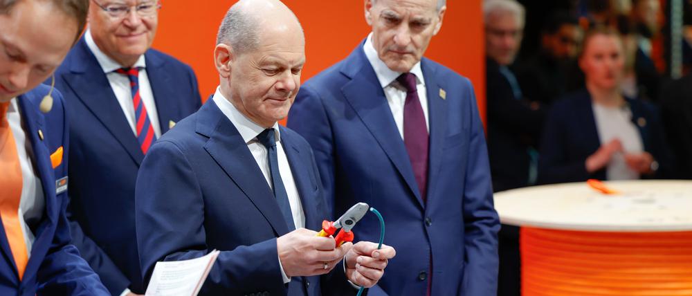 Bundeskanzler Olaf Scholz (SPD) schneidet ein Stück einer Datenleitung aus einem nachhaltigen, biobasierten Mantelmaterial zur industriellen Anwendung ab am Stand von Lapp auf der Hannover Messer.