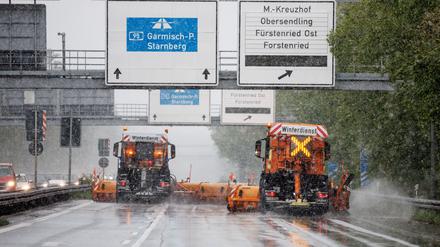 Zwei Fahrzeuge vom Winterdienst fahren bei Schneefall über die Autobahn 95 in München.