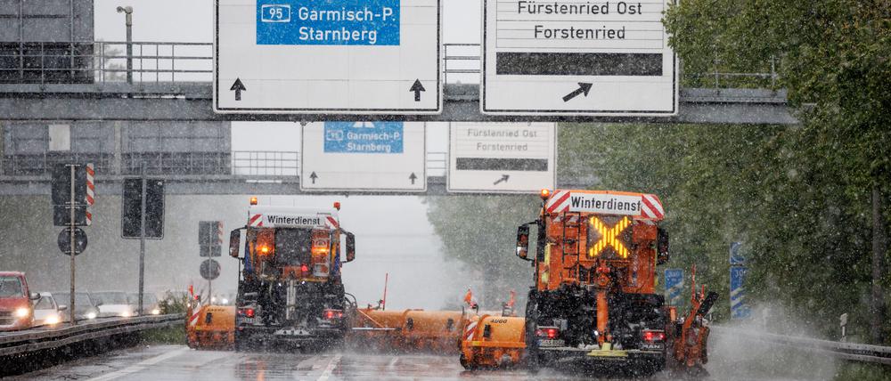 Zwei Fahrzeuge vom Winterdienst fahren bei Schneefall über die Autobahn 95 in München.
